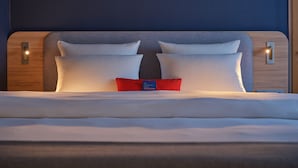 Een net opgemaakt bed met witte lakens en twee kussens, een rood accentkussen, en een blauw label in het midden.