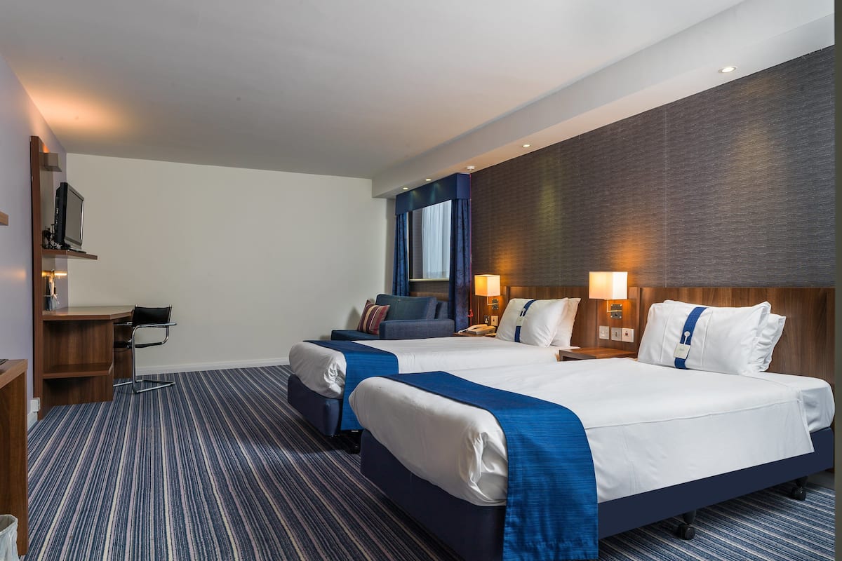 A hotel room with two beds, a desk, and a chair.