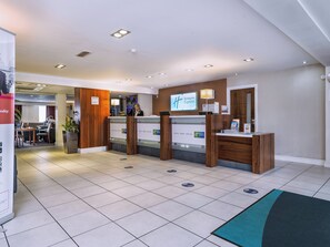 A hotel reception area with a reception desk, a waiting area, and a visible dining section.