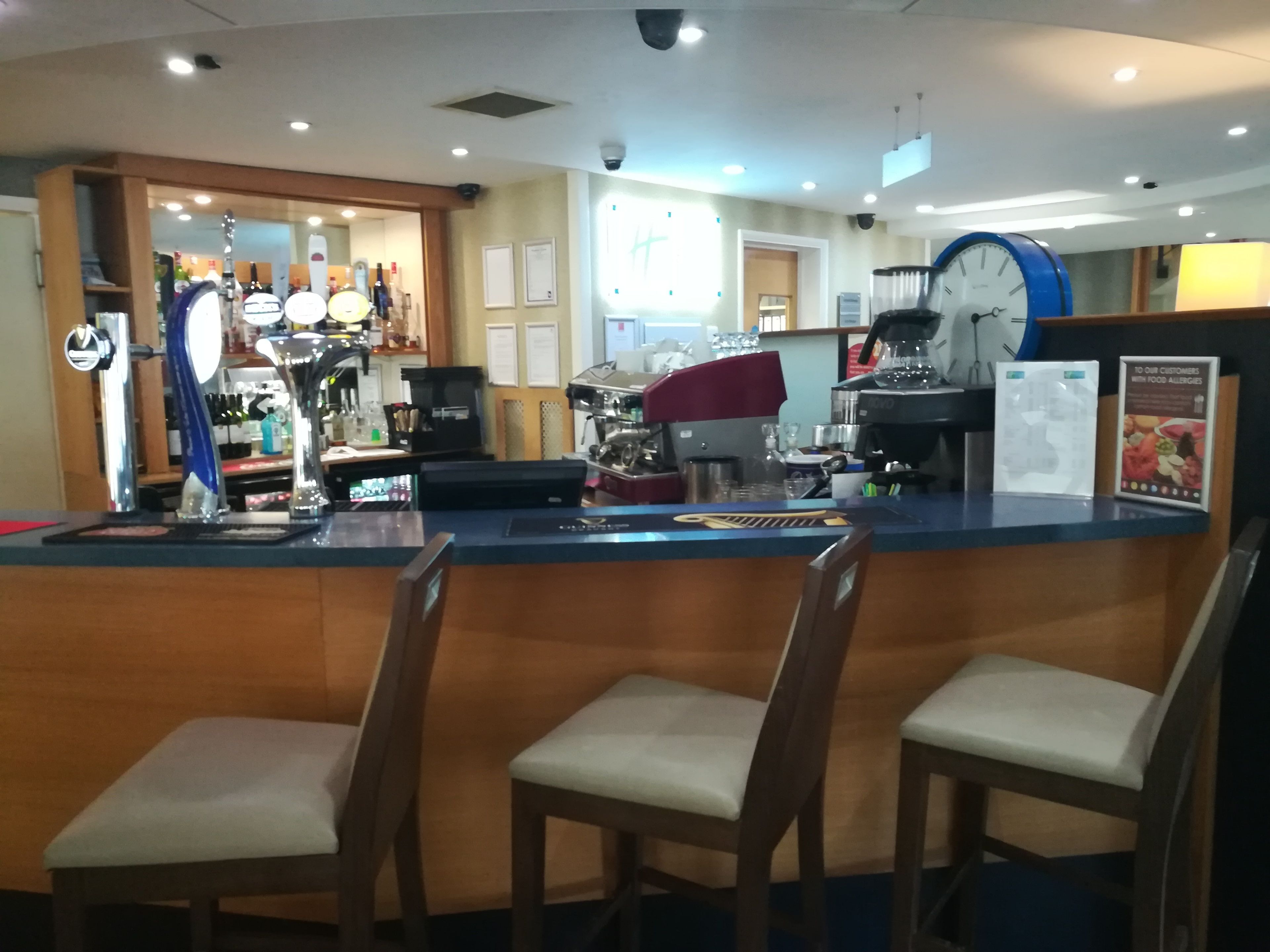 A bar area with a counter, two bar stools, a clock, and a menu board.