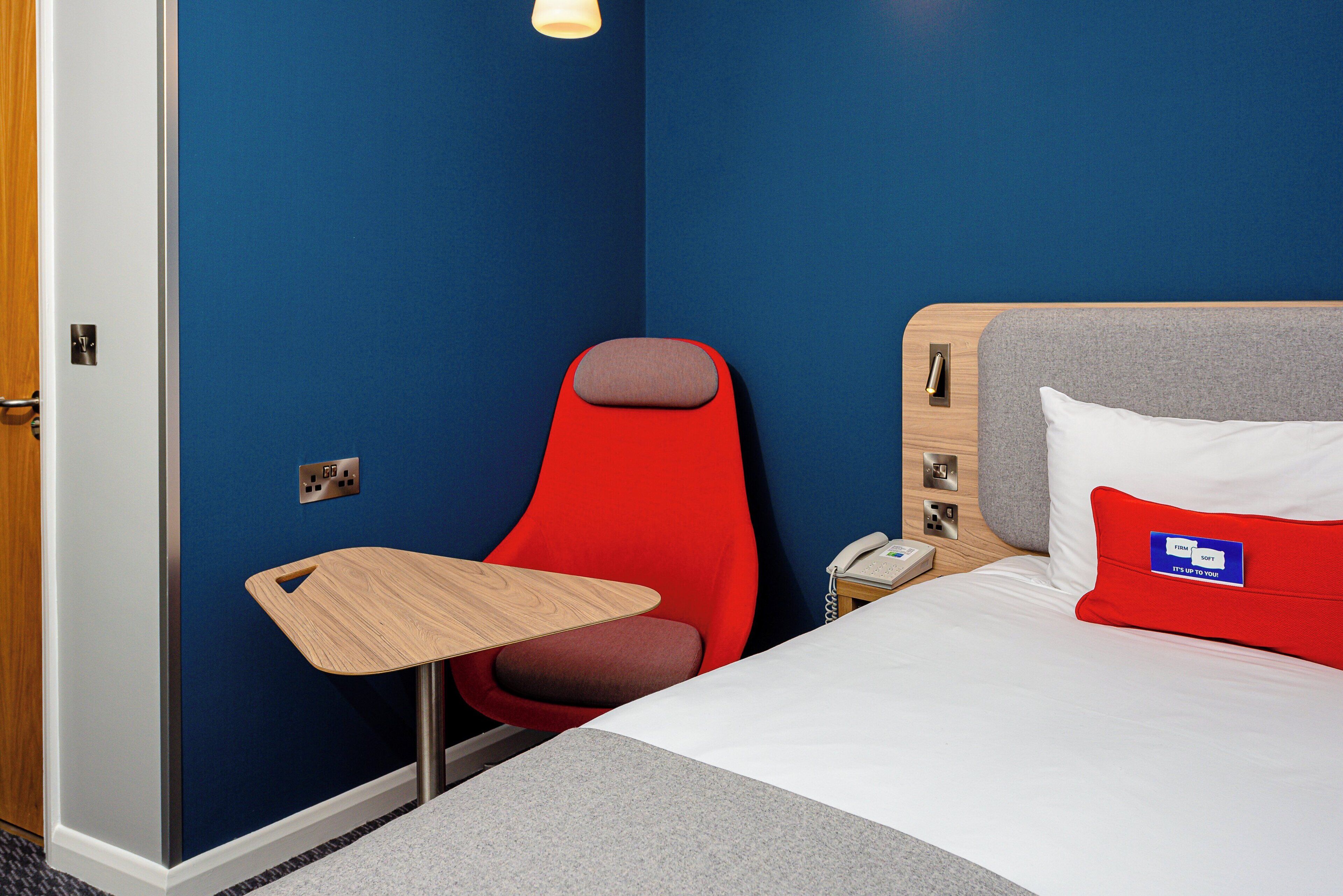 A hotel room with a bed, a small table, a chair, and a bedside telephone.