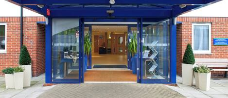 A hotel entrance with a blue canopy, glass doors, and potted plants.