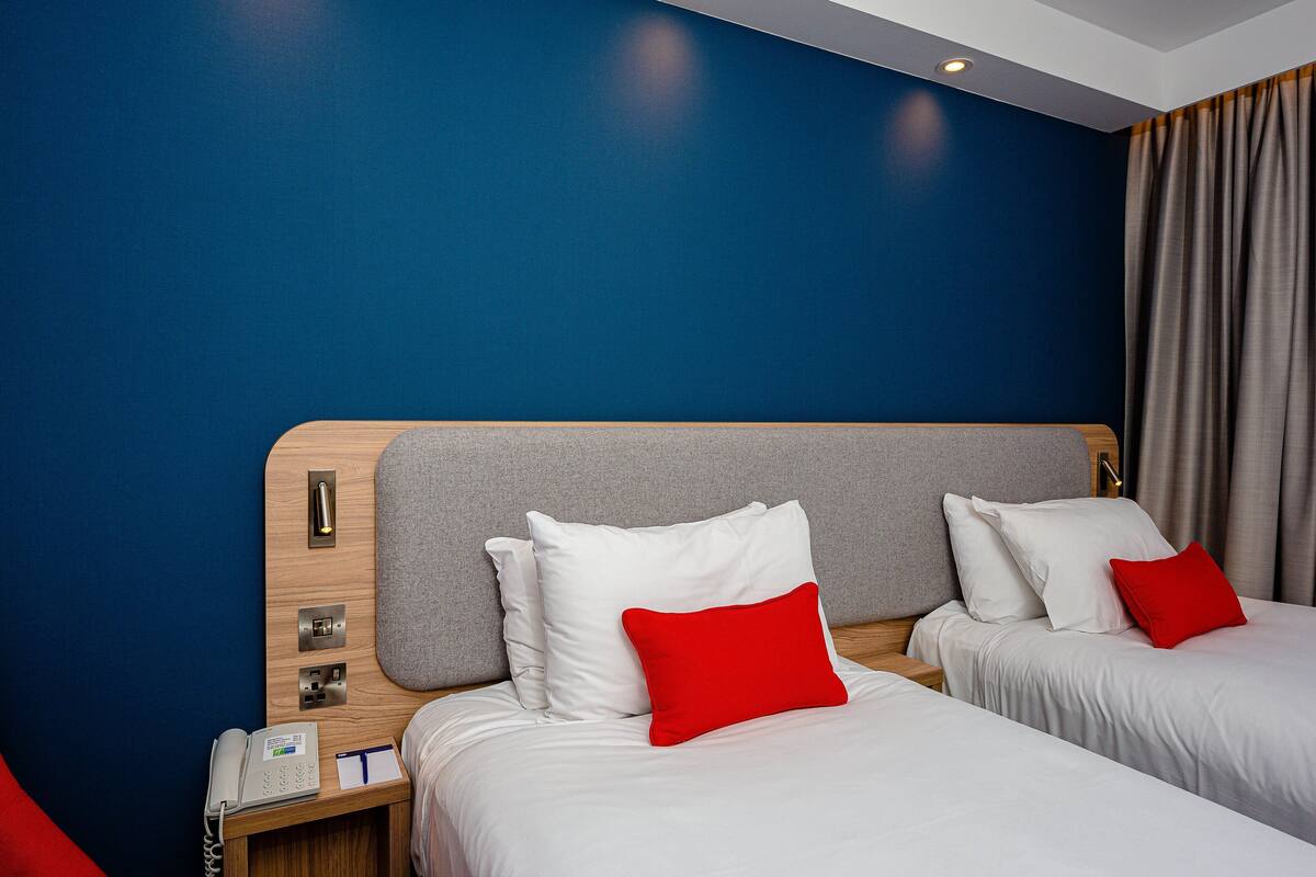 A hotel room with two beds, a wooden headboard, a bedside phone, and a red pillow.