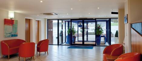 A hotel lobby with red chairs, a blue mat, and a glass door entrance.