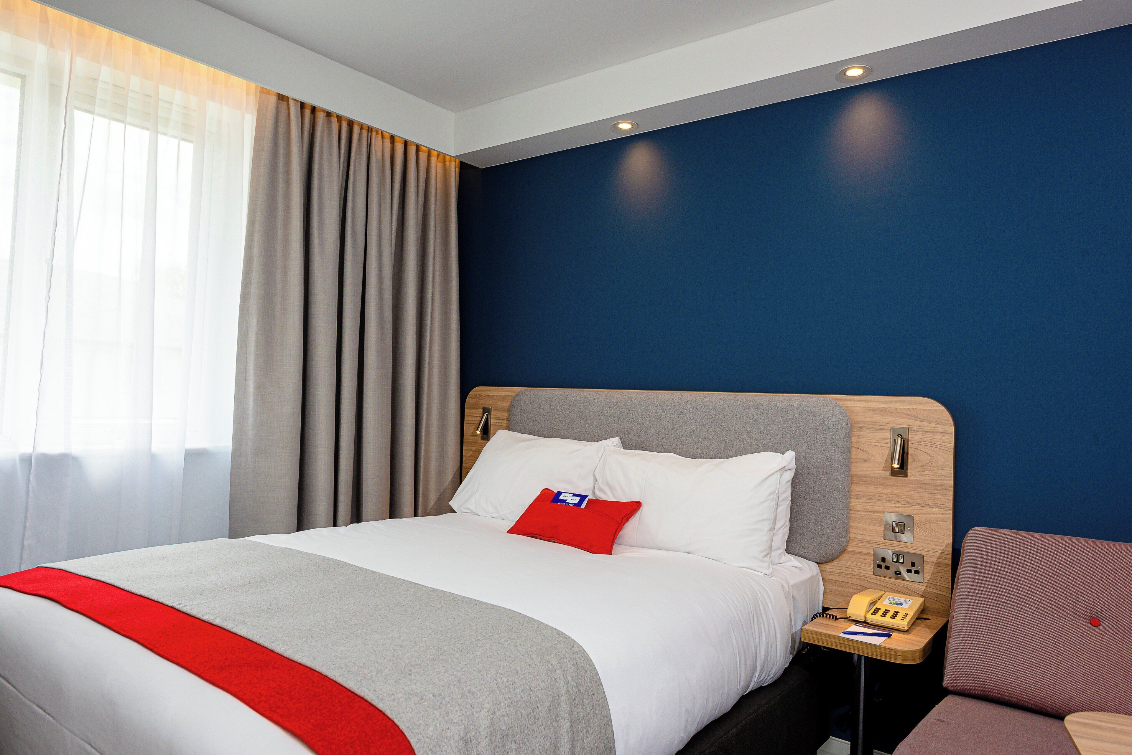 A hotel room with a bed, a bedside table with a phone, and a chair.