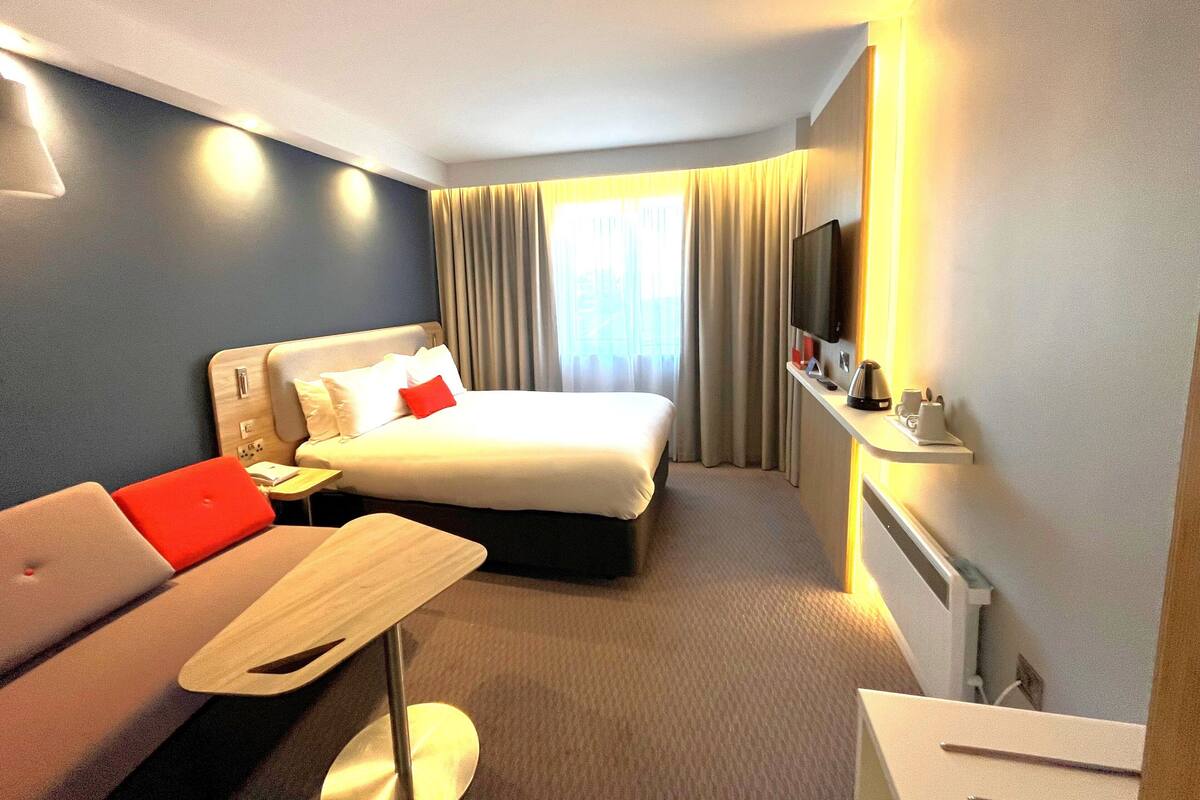 A hotel room with a bed, a desk, a TV, and a view of the outdoors.