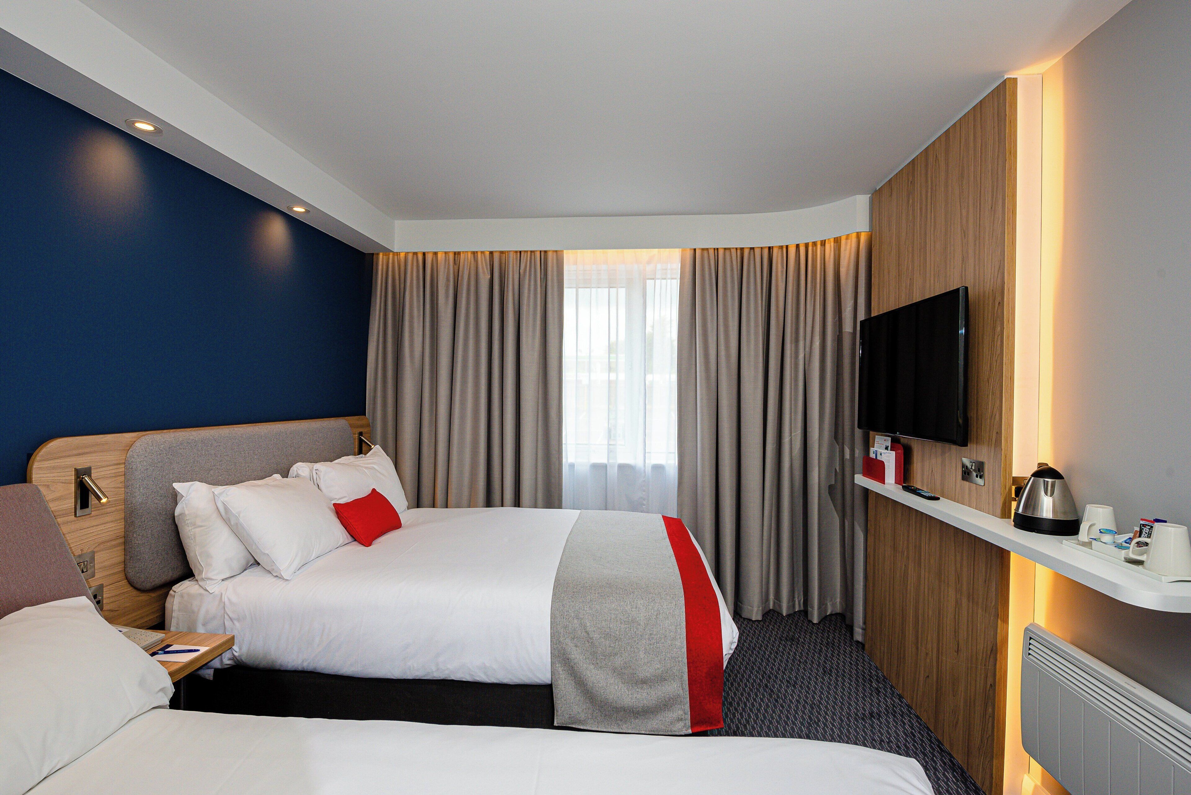 Ein Hotelzimmer mit zwei Betten, einem Fernseher, einer Kaffeemaschine und einem kleinen Tisch.