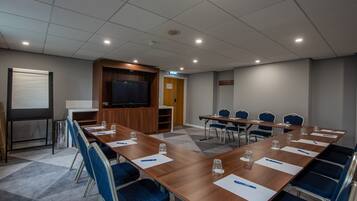 A conference room with a long table, blue chairs, and a projector screen.