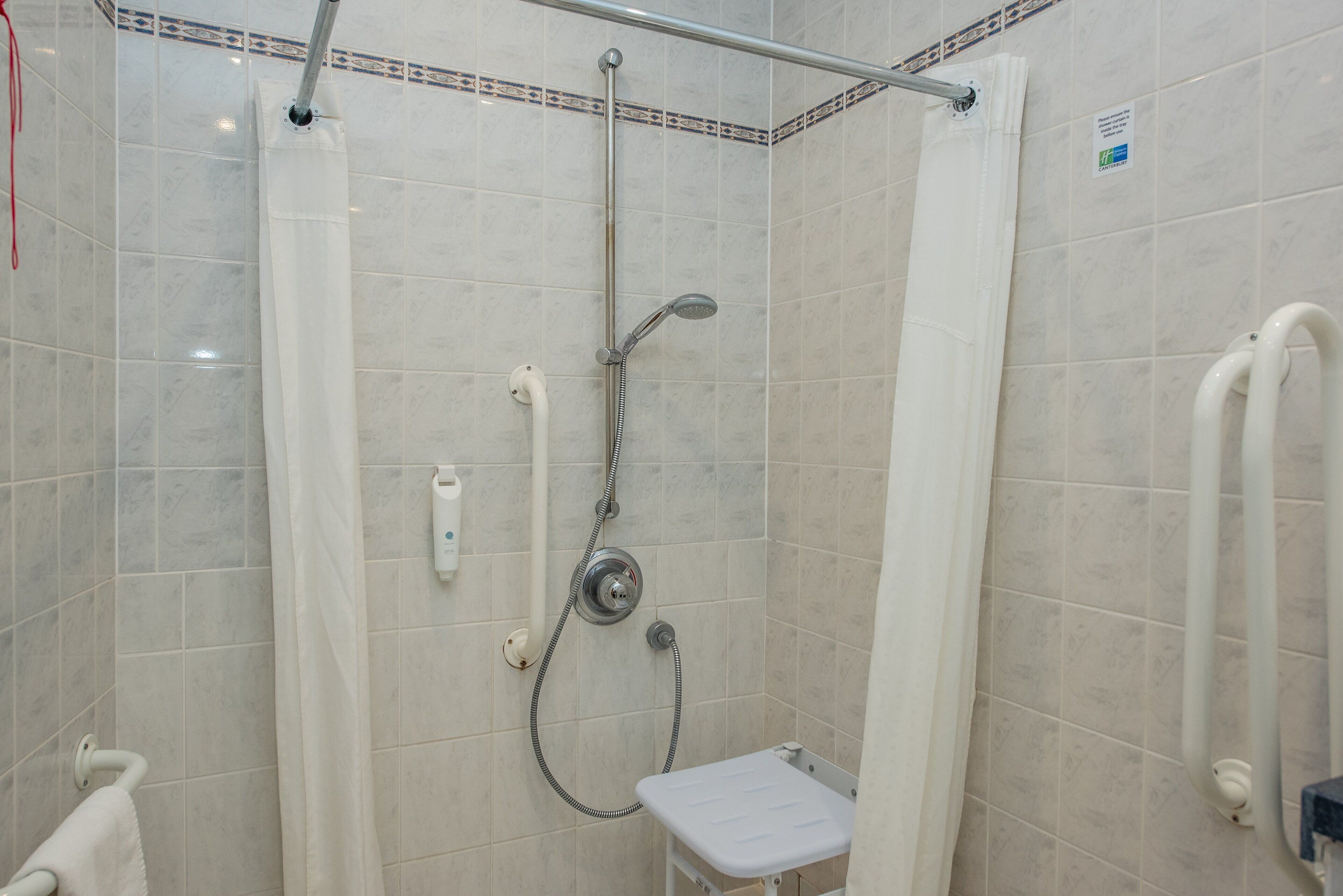 A small, enclosed shower area with a handheld showerhead, a handheld shower attachment, and a white shower seat.