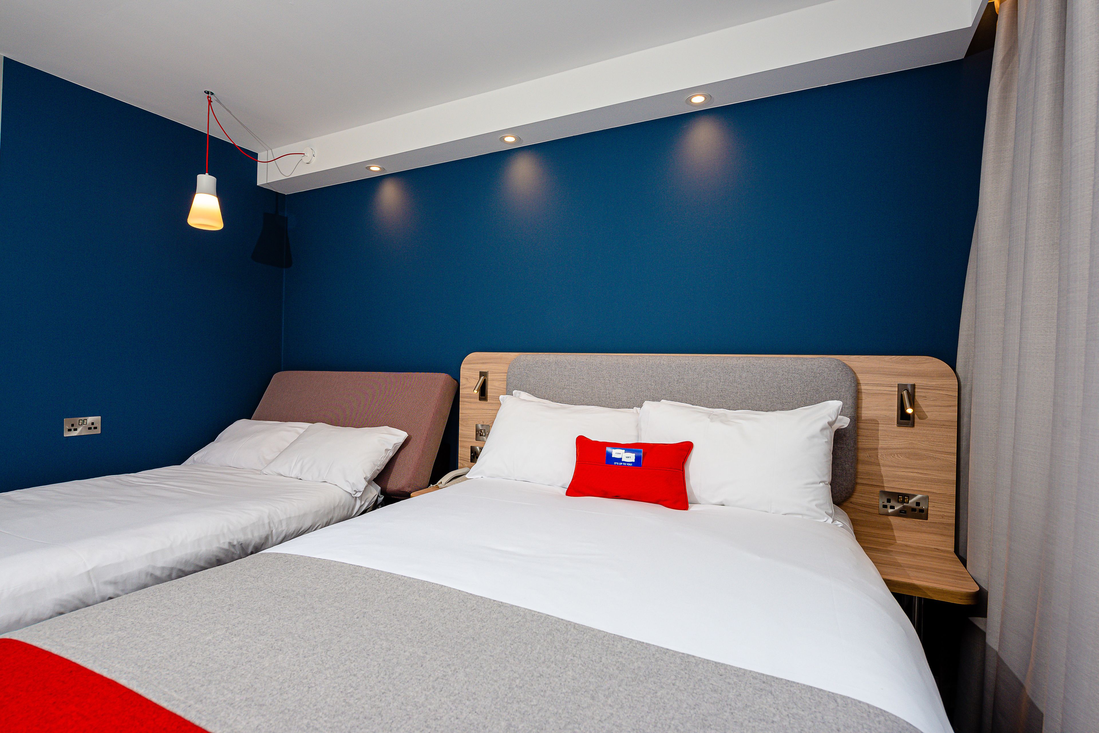 Habitación de hotel con dos camas, un almohadón rojo y una lámpara colgante.