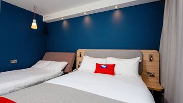 Habitación de hotel con dos camas, un almohadón rojo y una lámpara colgante.