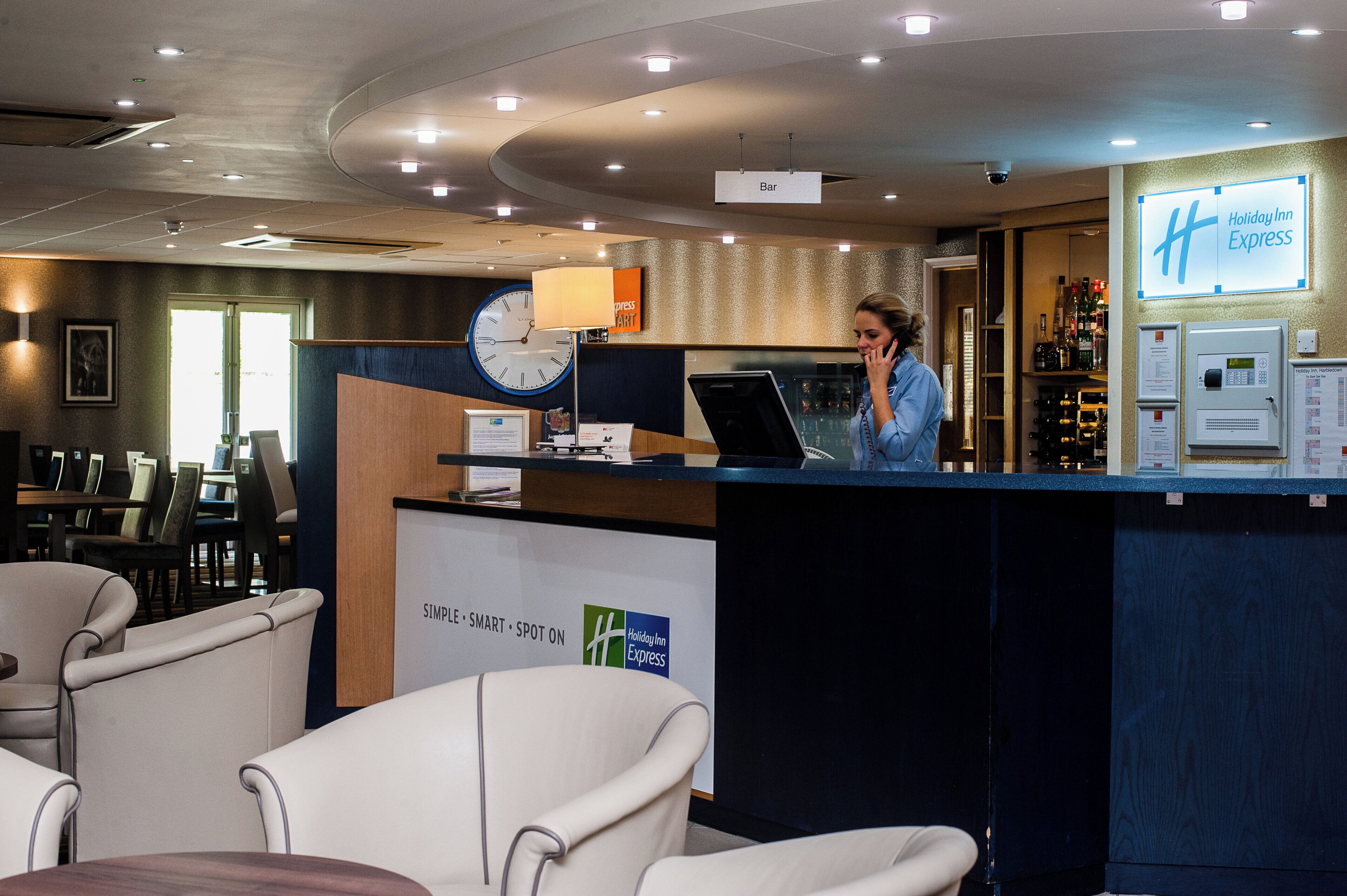 Zona de recepción de un hotel con un reloj, un letrero de bar y un letrero de Holiday Inn Express.