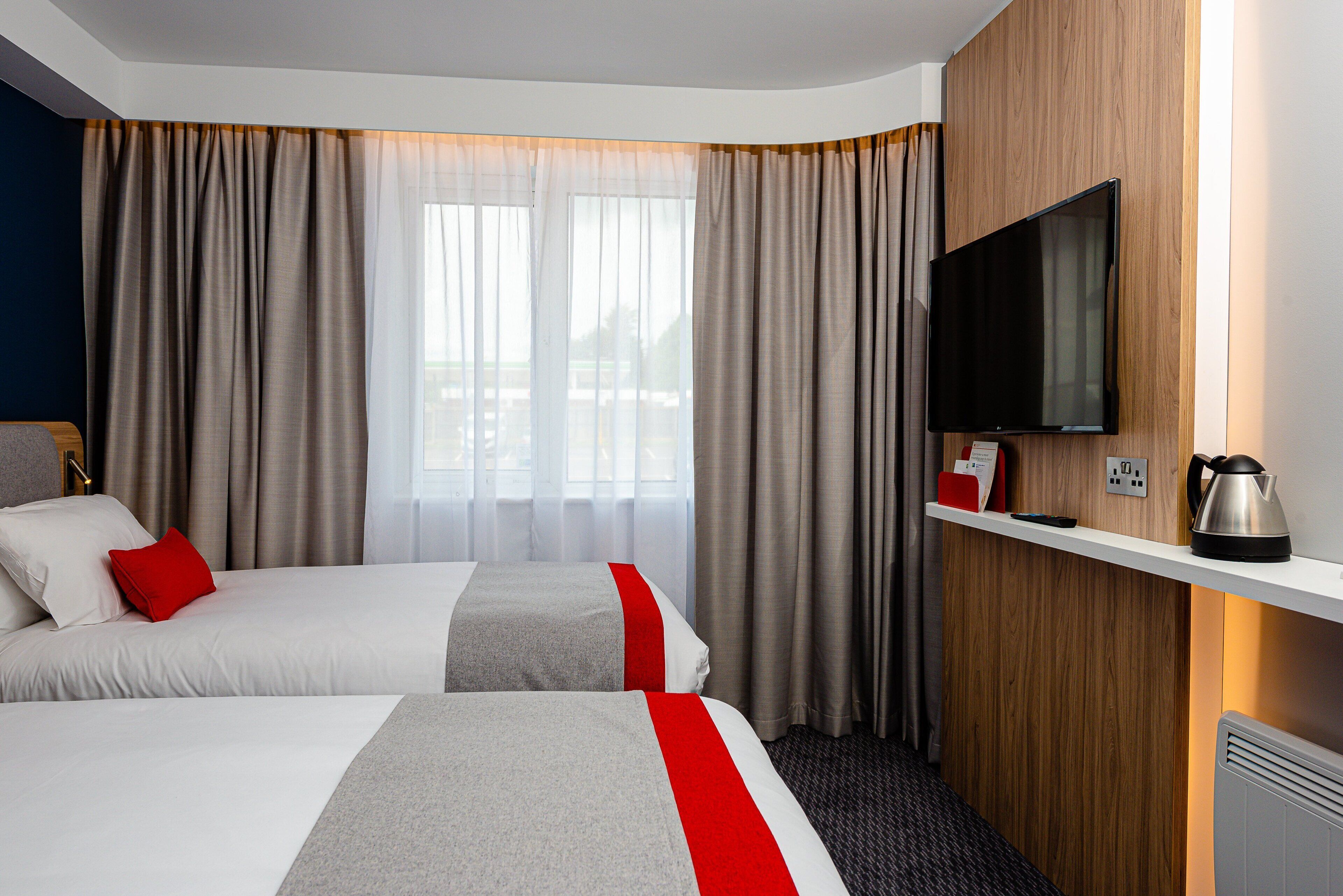 Ein Hotelzimmer mit zwei Betten, einem Fernseher, einer Kaffeemaschine und einem Fenster mit Vorhängen.