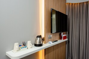 Habitación de hotel con un estante blanco que sostiene una cafetera, tazas y un control remoto.