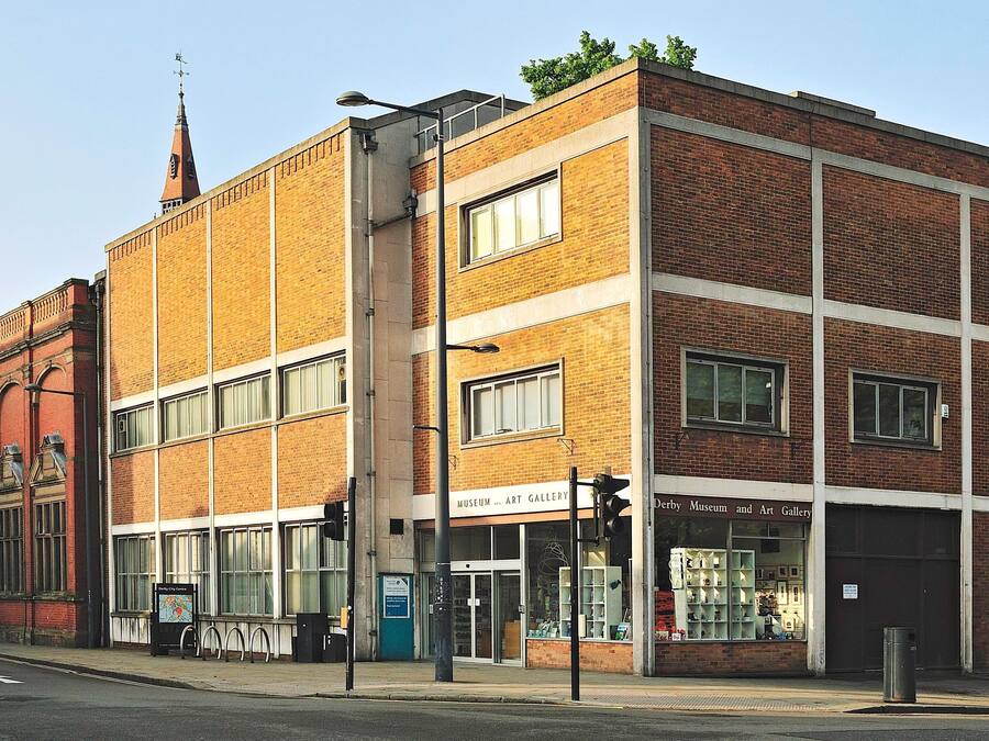 A multi-story brick building with large windows and a sign for the Derby Museum and Art Gallery.