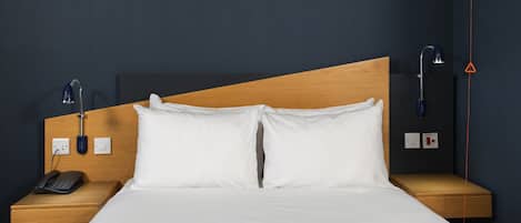 A hotel room with a wooden headboard, white bedding, a bedside phone, and a lamp.