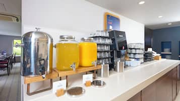 Una barra de desayuno con dispensadores de jugo, una máquina de café y un letrero que dice '¡DESPIERTA!'
