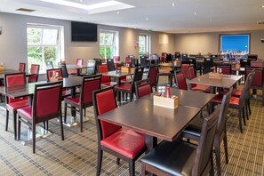 Une salle de conférence équipée de plusieurs tables et chaises, de grandes fenêtres et d’un téléviseur à écran plat fixé au mur.