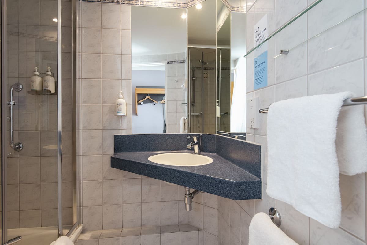 A modern bathroom with a glass-enclosed shower, a sink with a dark countertop, and a white towel hanging on a rack.