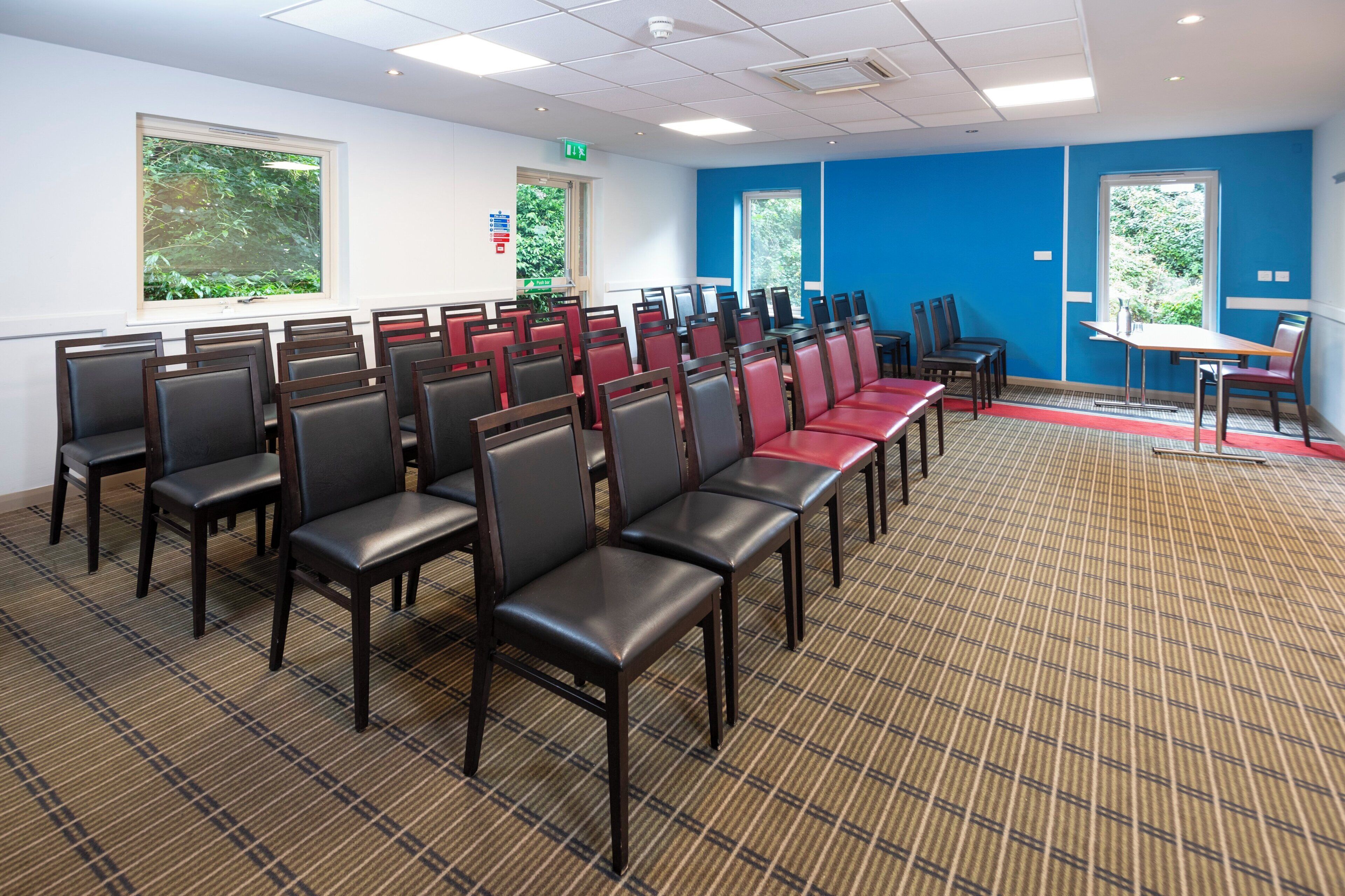 A conference room with rows of chairs, a table, and windows with greenery outside.