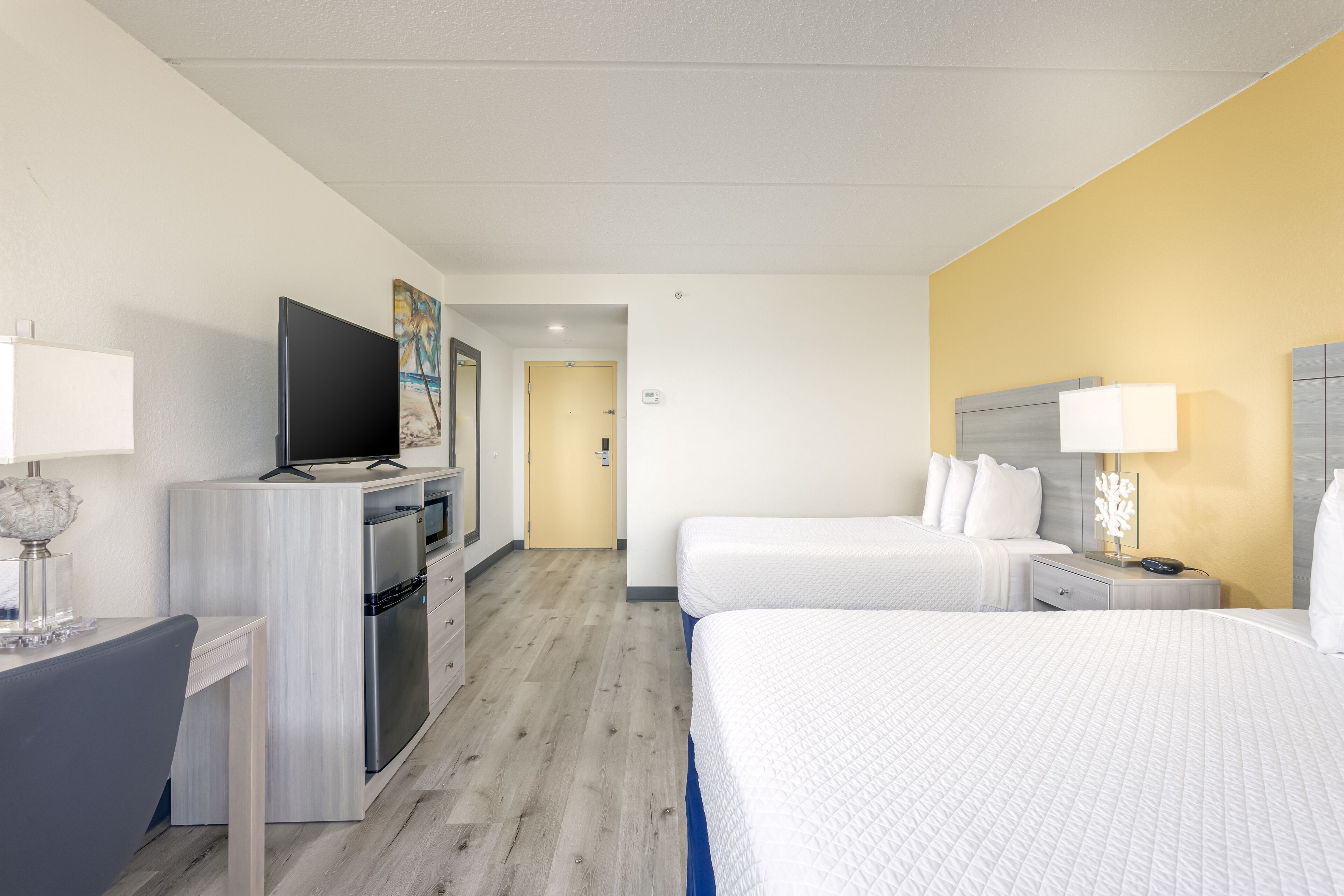 Une chambre d’hôtel équipée d’une kitchenette, d’une télévision, d’un lit, d’une table de chevet avec une lampe et d’une porte donnant sur une autre pièce.