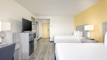 Une chambre d’hôtel équipée d’une kitchenette, d’une télévision, d’un lit, d’une table de chevet avec une lampe et d’une porte donnant sur une autre pièce.