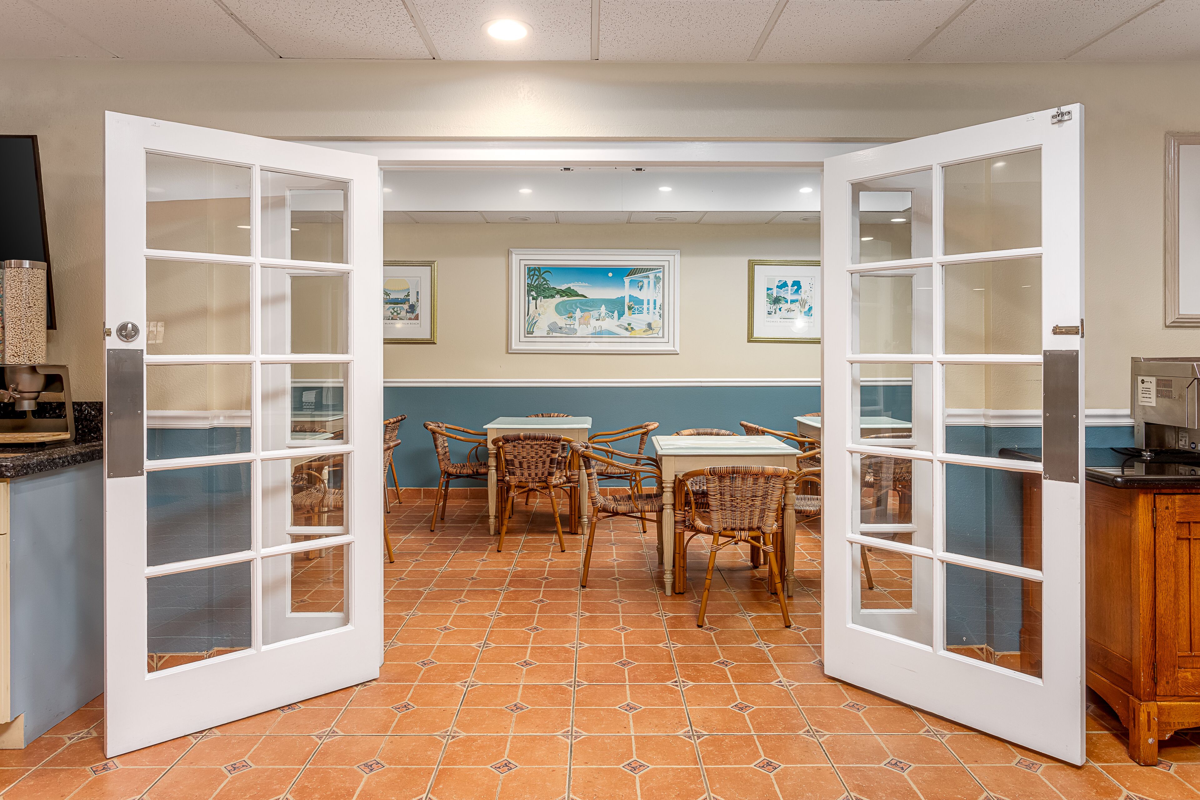 A dining area with open doors, wicker chairs, and a tiled floor.