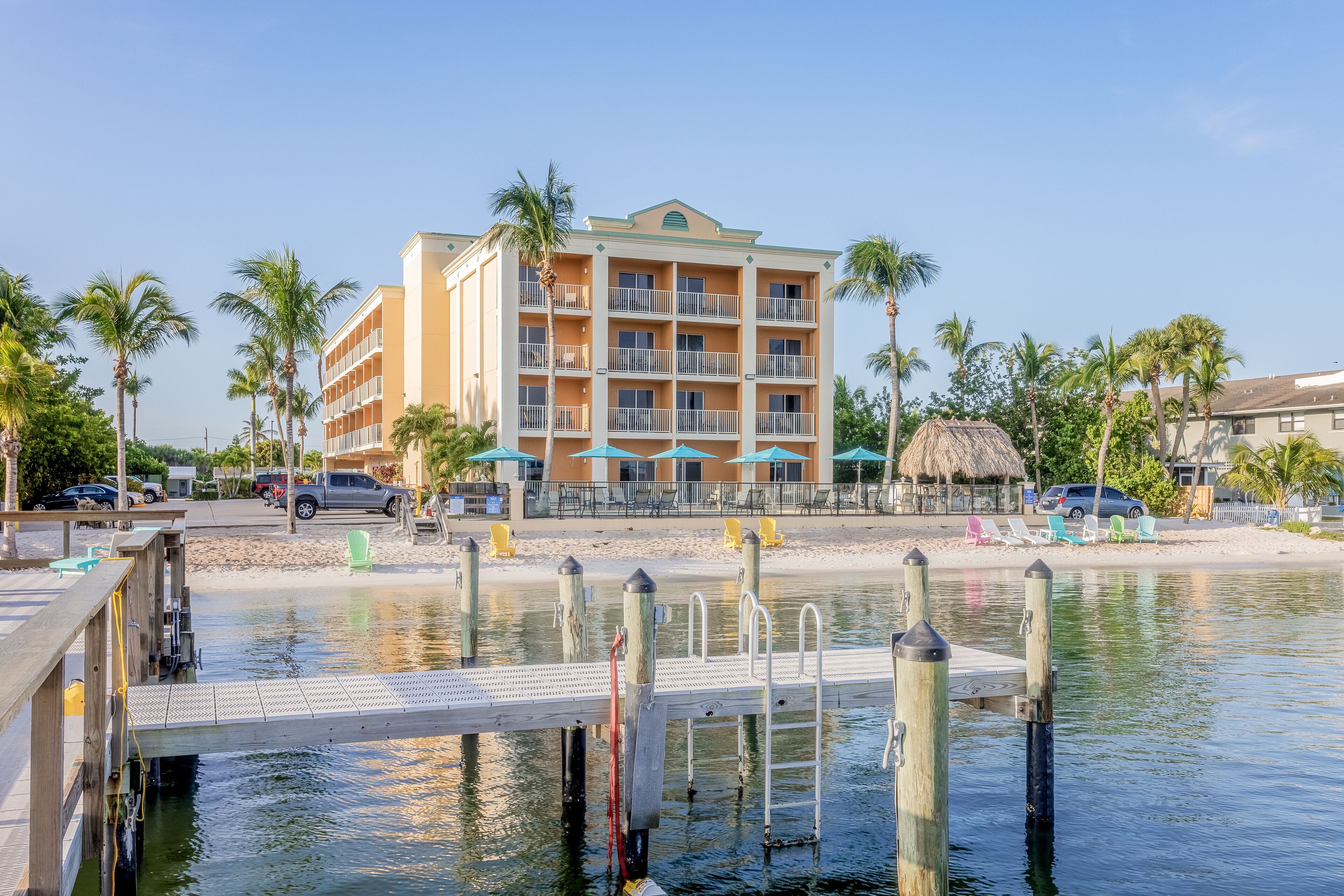 A waterfront hotel with a dock, palm trees, and beach chairs.