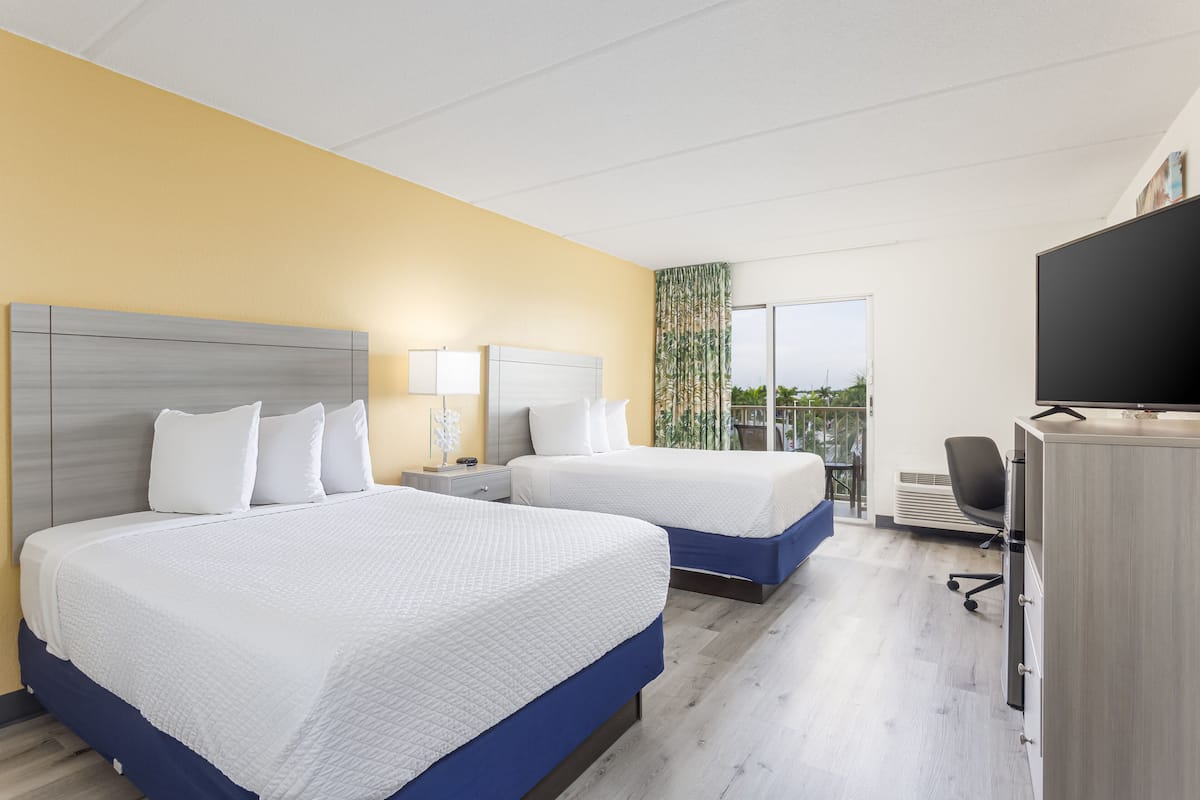 A hotel room with two beds, a desk, a television, and a balcony with a view.