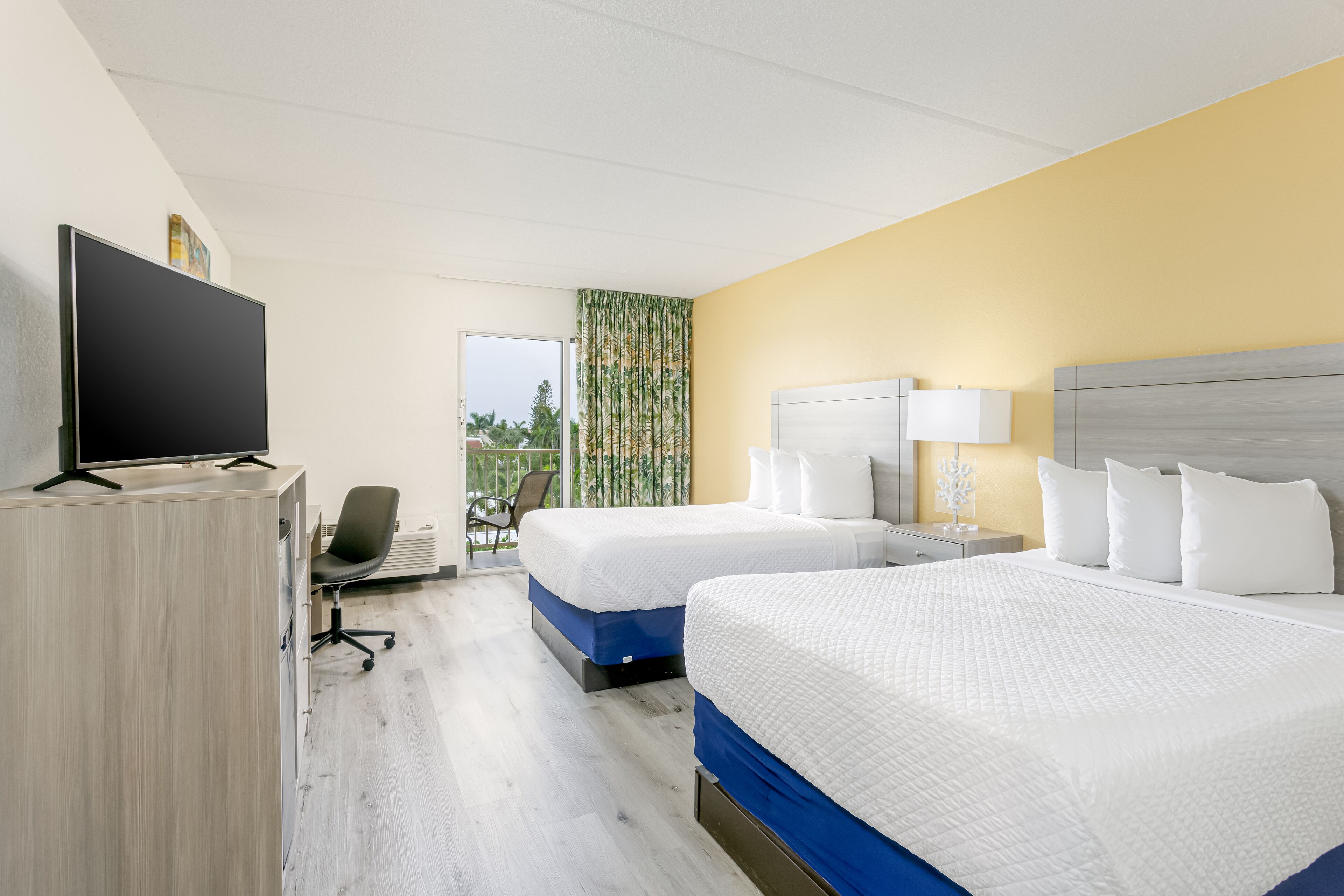 Une chambre d’hôtel avec deux lits, un bureau avec un ordinateur et une chaise.
