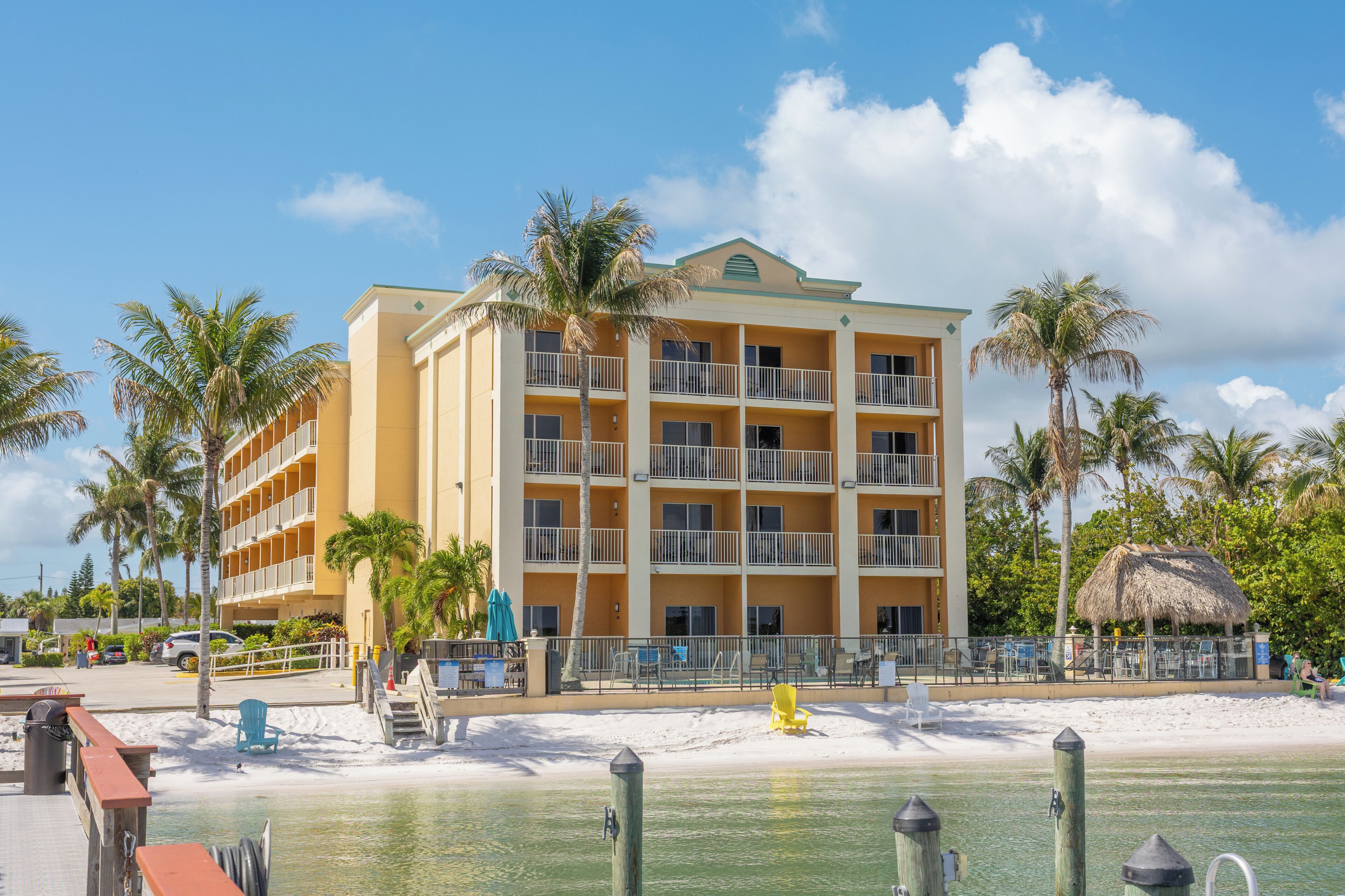 A multi-story hotel with balconies, a beach view, and palm trees.