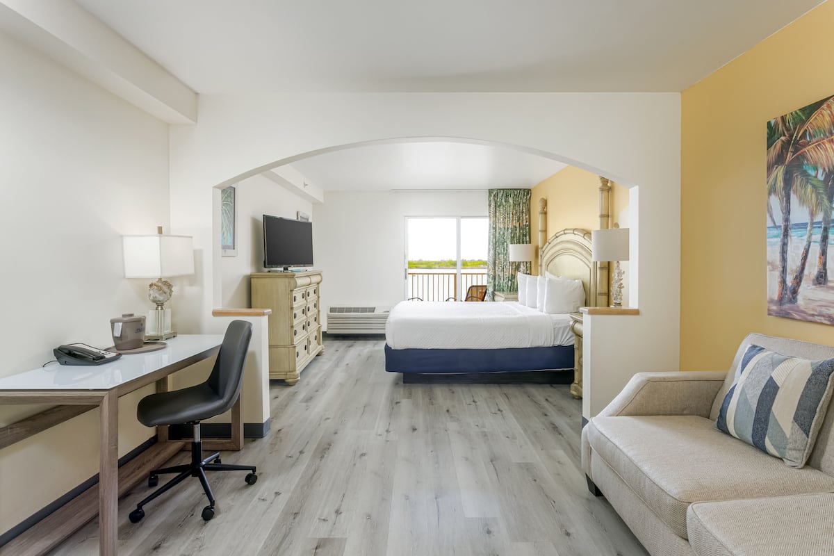 A hotel room with a desk, chair, bed, and a view of the outdoors.