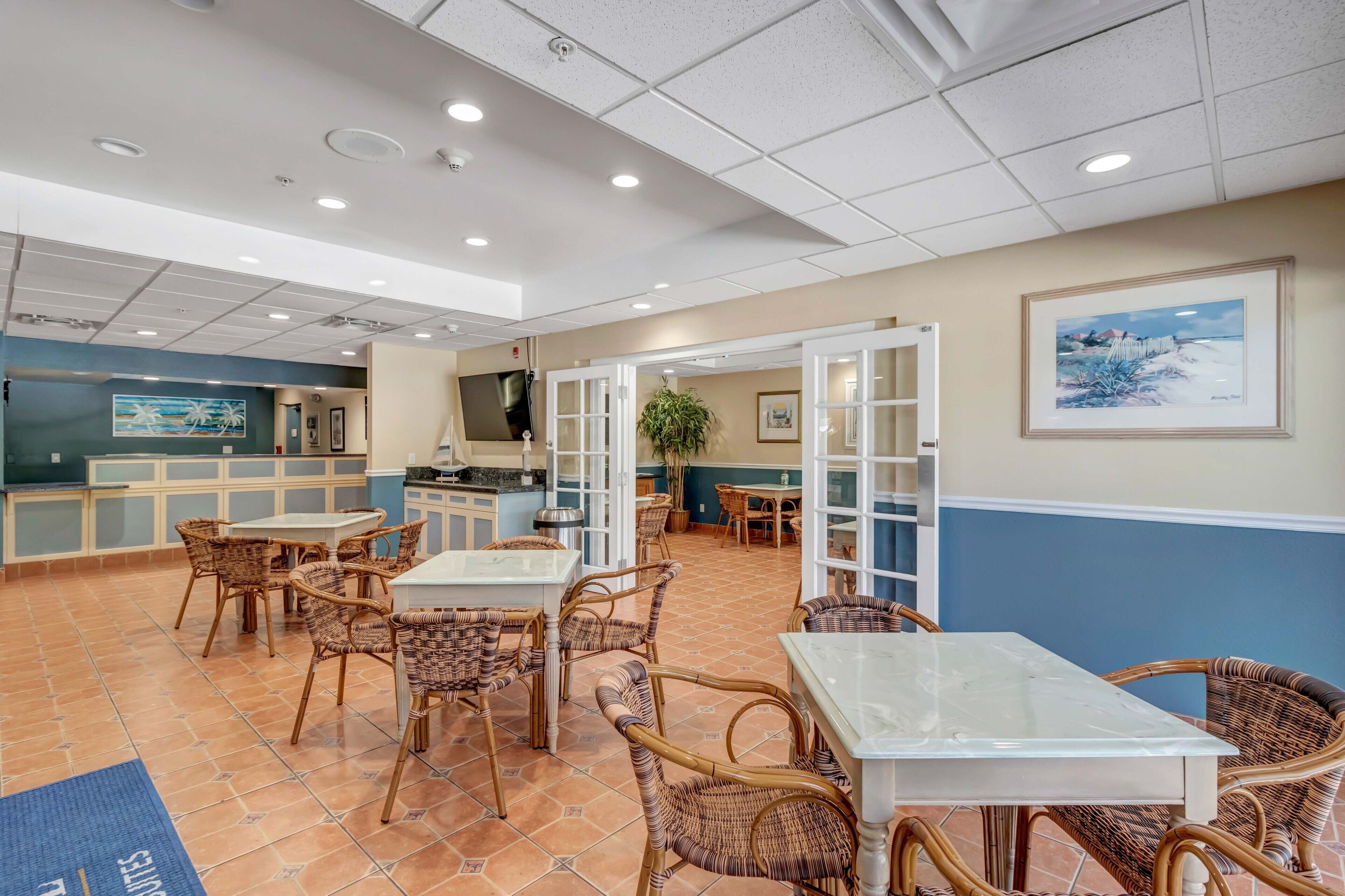 A hotel lobby with wicker furniture, a kitchen area, and a painting on the wall.