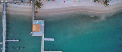 An aerial view of a beach with a dock, a pool, and several boats.