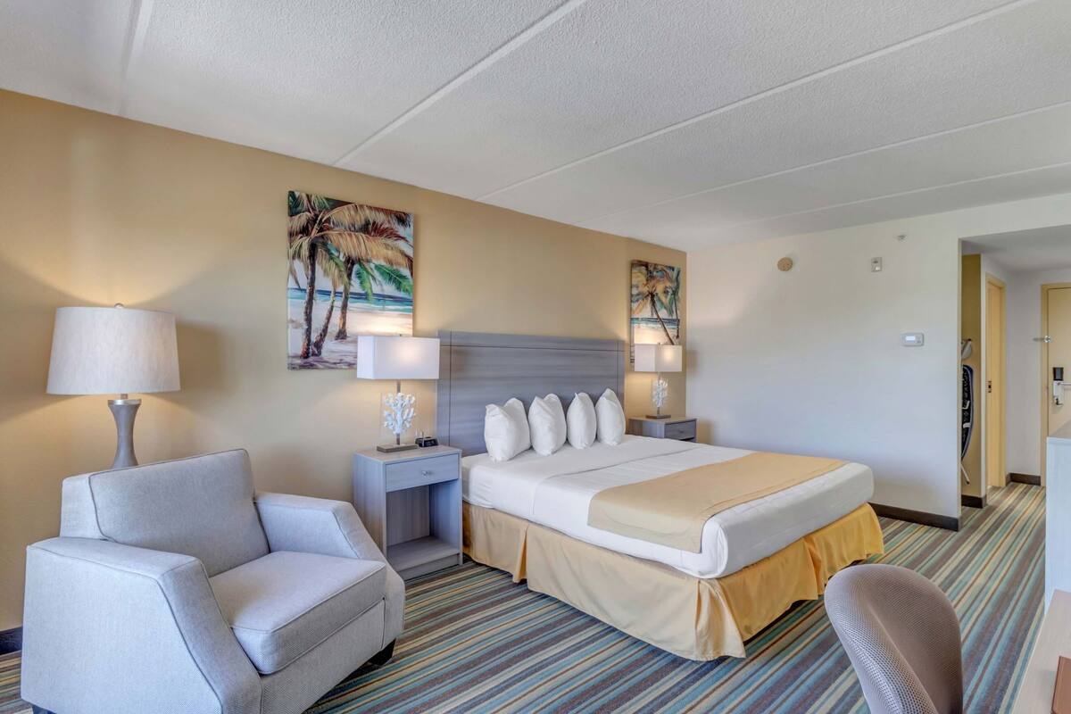 A hotel room with a bed, two bedside tables with lamps, a chair, and a painting on the wall.