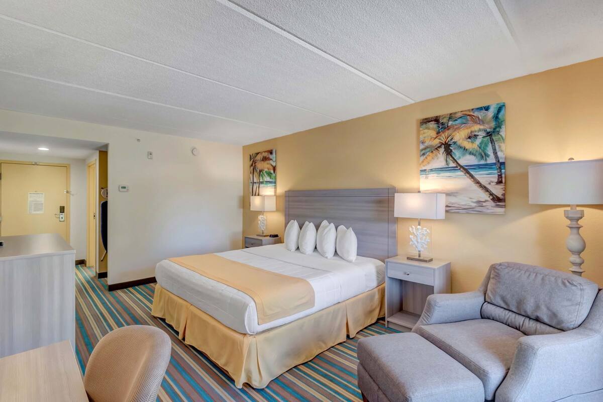 A hotel room with a large bed, a desk, a chair, and a painting on the wall.
