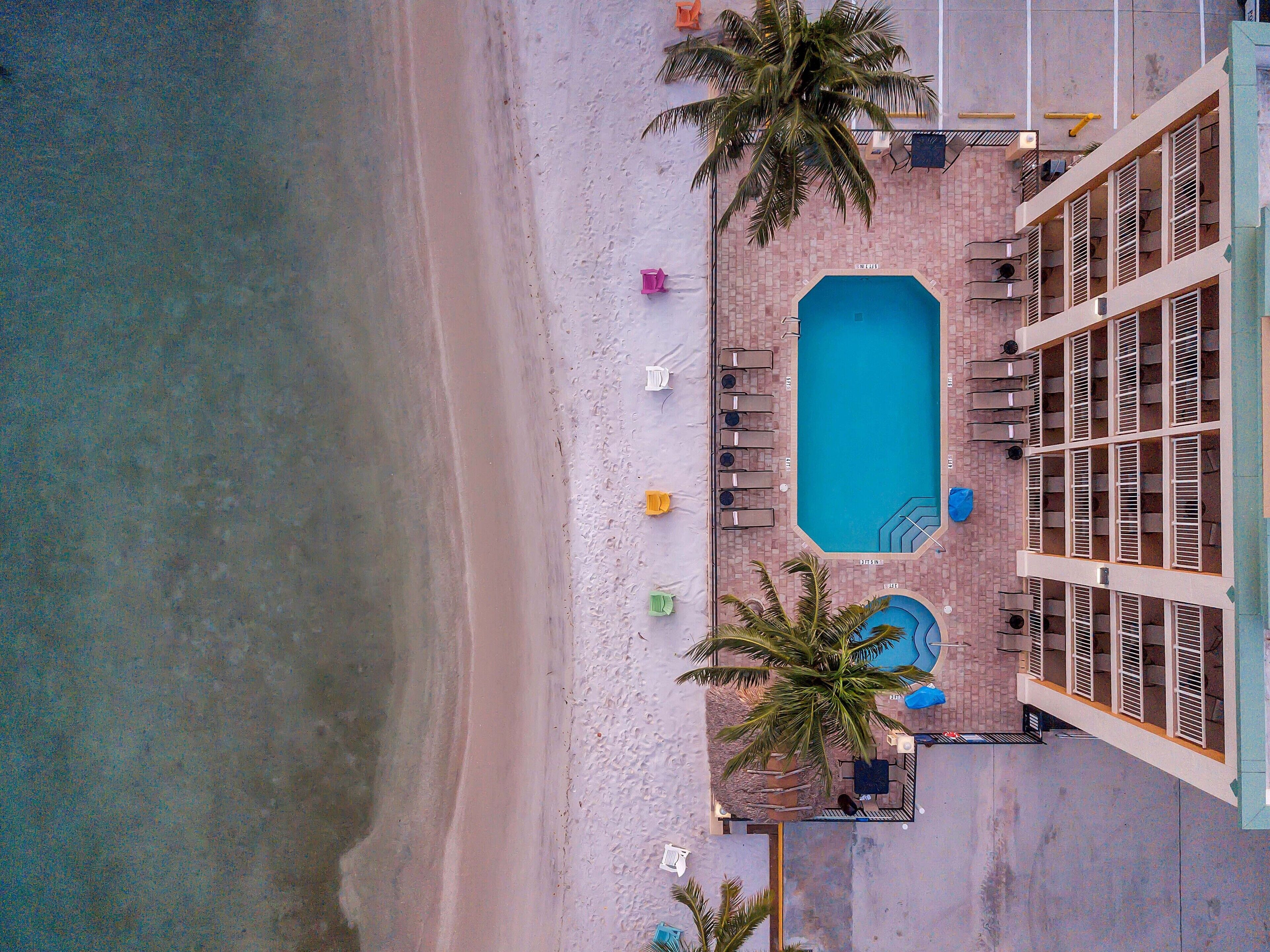 Vista aerea di un hotel con piscina, sdraio e palme.
