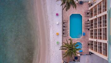 An aerial view of a hotel with a swimming pool, beach chairs, and palm trees.