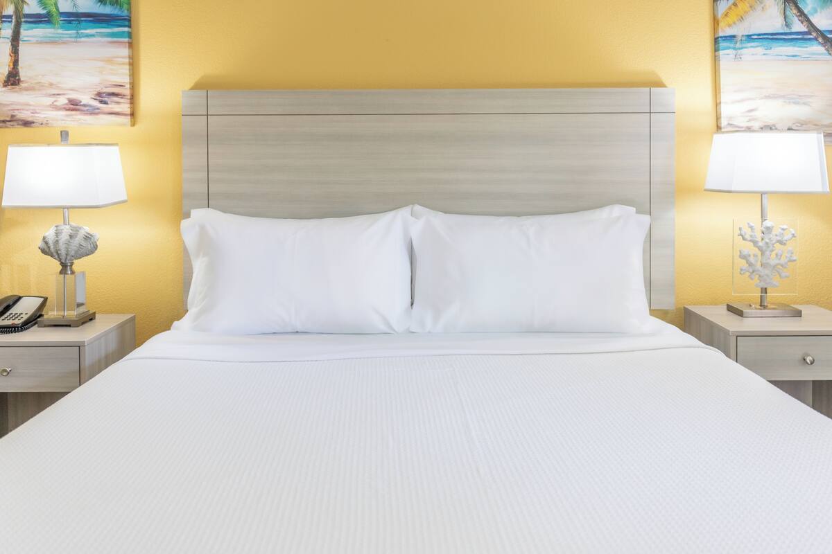 A hotel room with a large bed, two bedside tables, a nightstand, a lamp, and a painting on the wall.