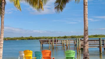 A beach with colorful Adirondack chairs, a wooden dock, and a clear blue sky.