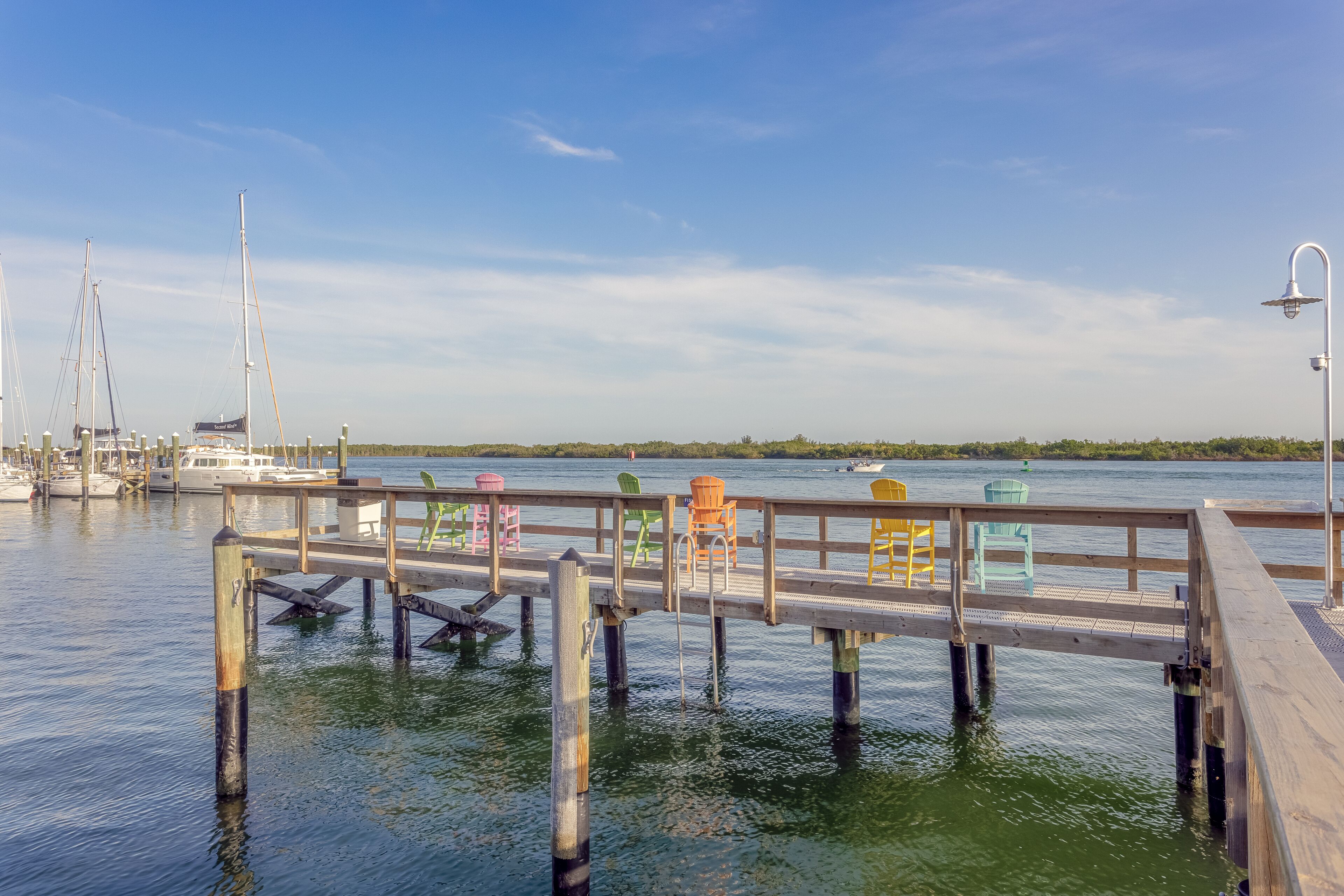 A wooden dock extending into calm waters with boats docked nearby and a clear sky above.