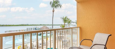 A balcony with a view of a swimming pool, palm trees, and a body of water.