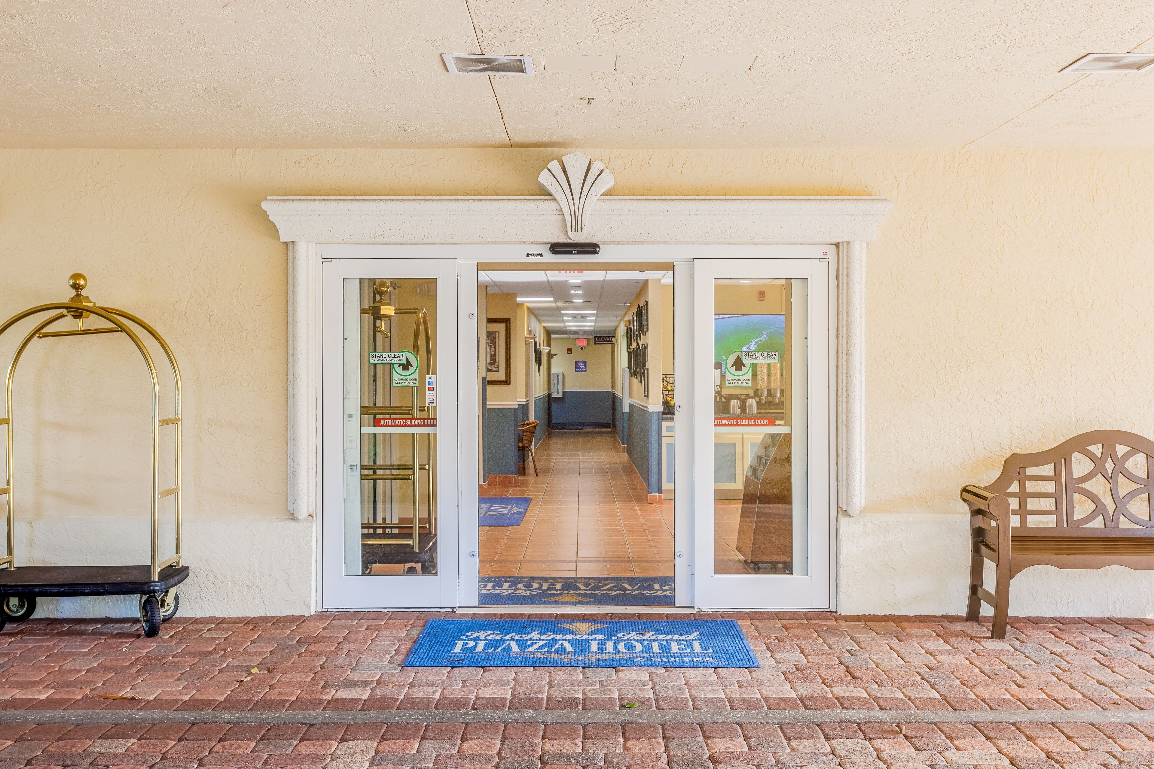 A hotel entrance with a blue doormat, a bench, and a cart.