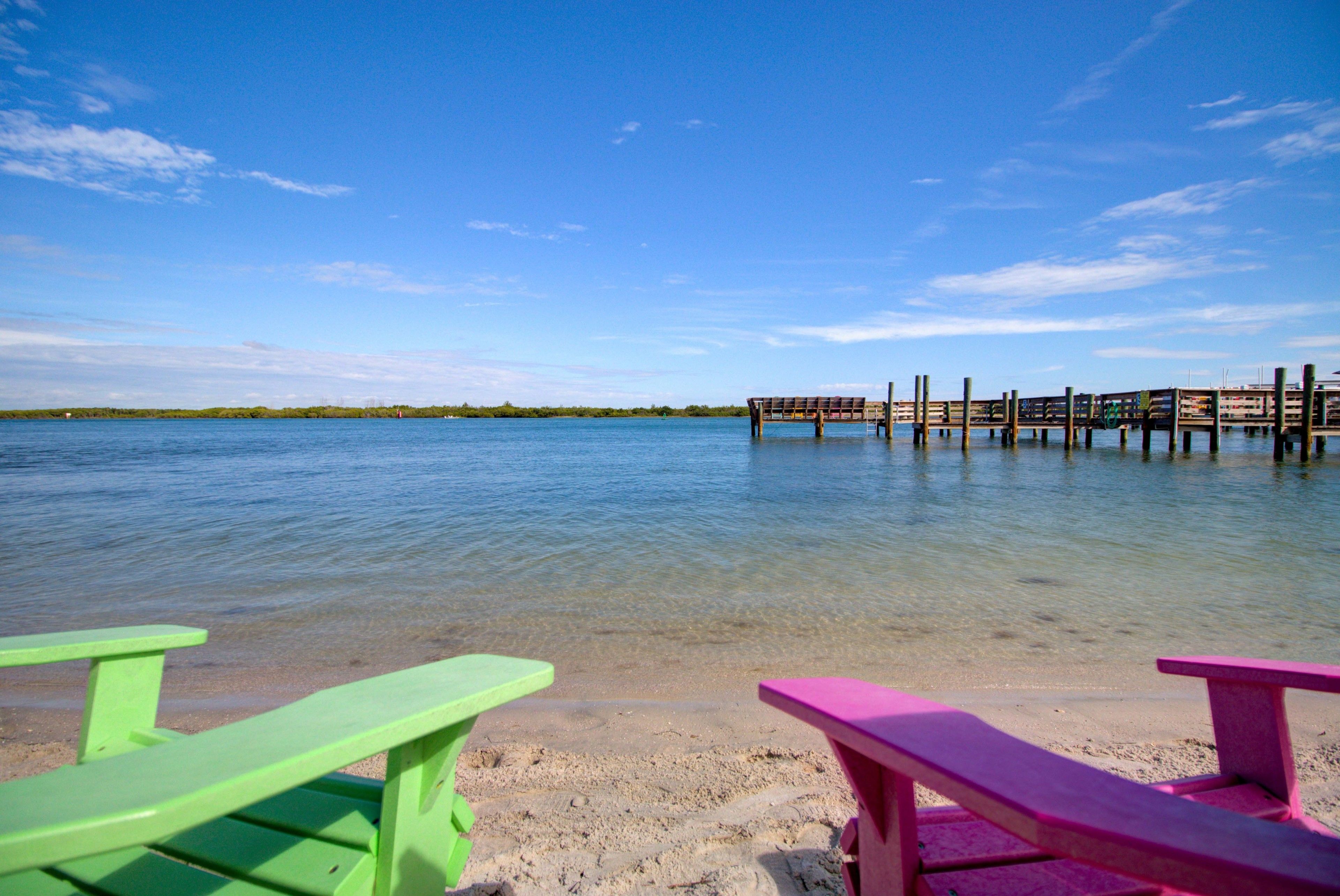 A beach with clear water, a wooden pier, and two picnic tables.