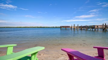 A beach with clear water, a wooden pier, and two picnic tables.