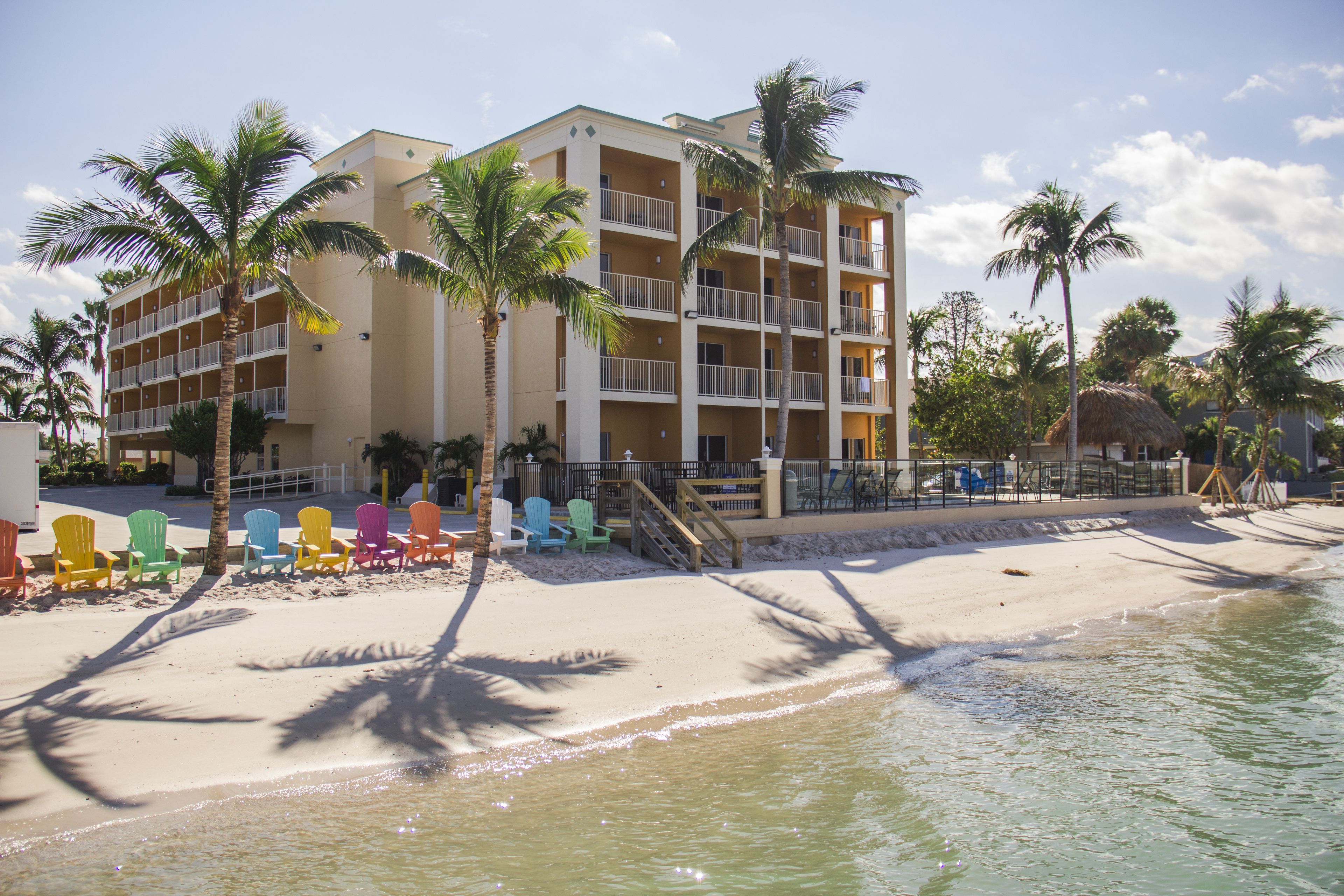 Ein Strandhotel mit mehreren Balkonen, einem Sandstrand und bunten Liegestühlen.