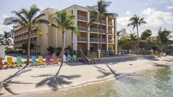 A beachfront hotel with multiple balconies, a sandy beach, and colorful beach chairs.