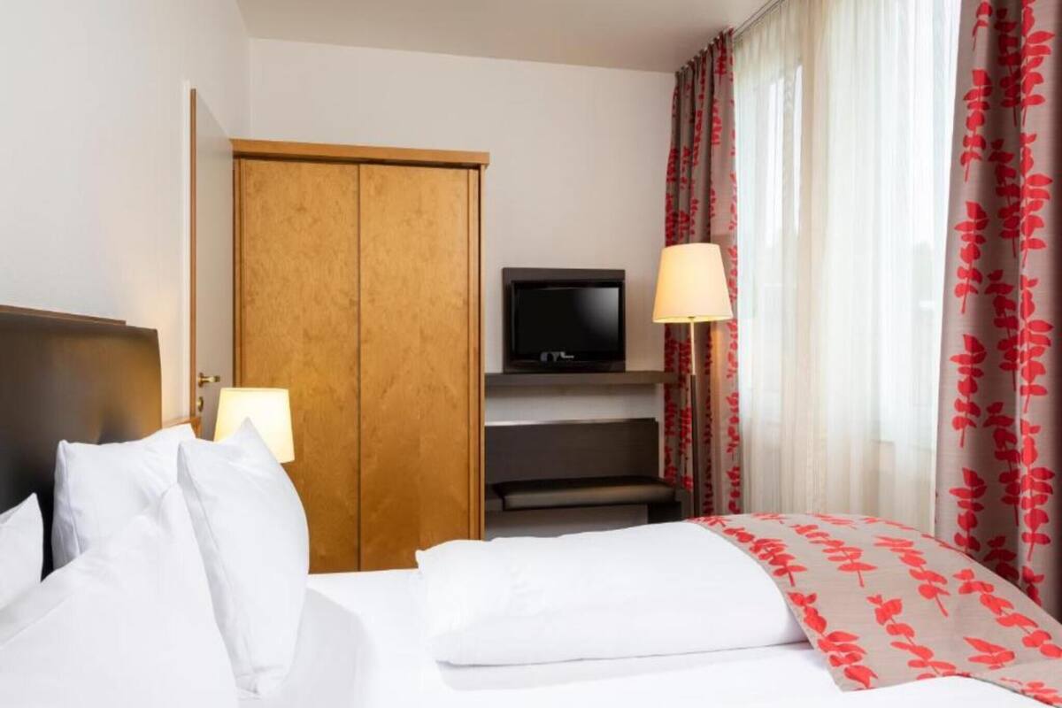A hotel room with a bed, a TV, a wardrobe, and a window with curtains.