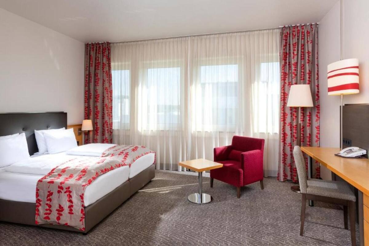 A hotel room with a bed, a desk, a chair, and a lamp.