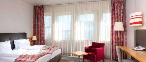 A hotel room with a bed, a desk, a chair, and a lamp.